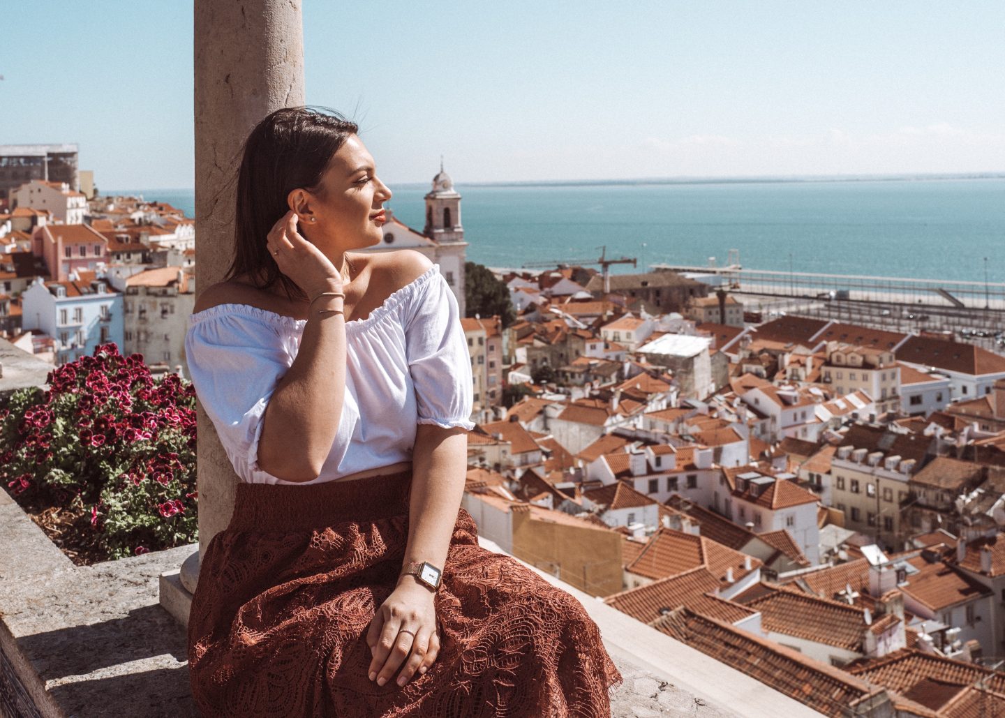 Mihaela sitting on a terrace overlooking Lisbon rooftops and the water