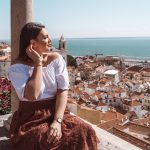 Mihaela sitting on a terrace overlooking Lisbon rooftops and the water